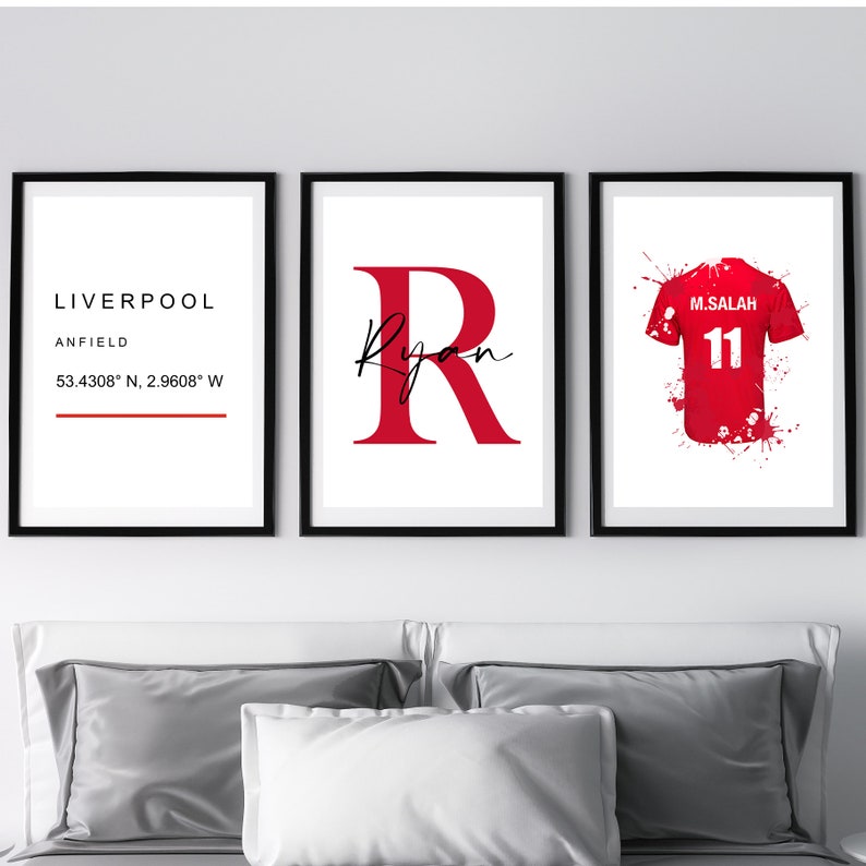 May include: Three framed prints with black borders. The left print says "LIVERPOOL ANFIELD 53.4308&deg; N, 2.9608&deg; W". The center print has a large red letter "R" with the name "Ryan" in script. The right print shows a red soccer jersey with "M.SALAH 11".