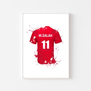May include: Red soccer jersey with the name "M. SALAH" and the number "11" in white. The jersey is depicted with red paint splatter effects on a white background.
