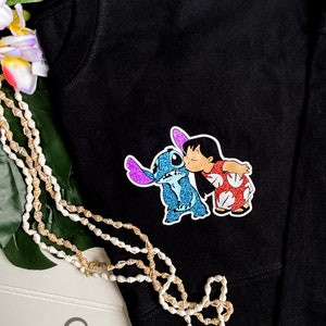 May include: Black t-shirt with a glittery blue Stitch and a red and white Lilo from the Disney movie Lilo & Stitch. The characters are kissing.