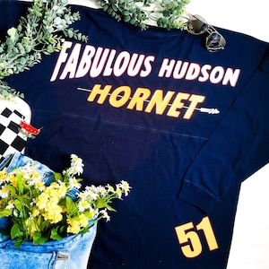May include: A navy blue long-sleeved shirt with the text "Fabulous Hudson Hornet" in yellow and red lettering. The number "51" is also printed in yellow on the sleeve.