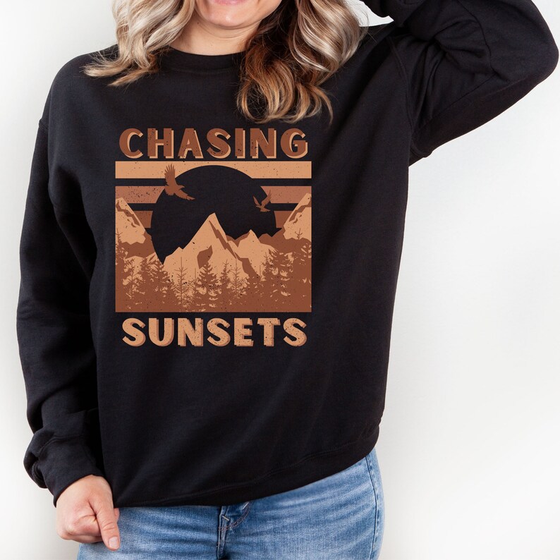 May include: A black sweatshirt with a brown graphic design featuring mountains, a sunset, and birds. The text "CHASING SUNSETS" is printed in brown letters.