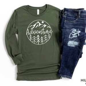 May include: A long-sleeved t-shirt in military green with a white graphic of a mountain range and trees in a circle with the word "Adventure" written in a script font.
