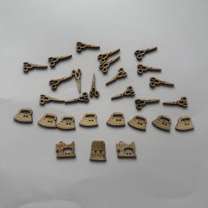 Könnte beinhalten: Eine Sammlung kleiner, hölzerner Verzierungen zum Thema Nähen. Das Sortiment umfasst Scheren, Bügeleisen, Nähmaschinen und Fingerhüte. Die Holzstücke sind hellbraun und auf einer hellgrauen Oberfläche angeordnet.