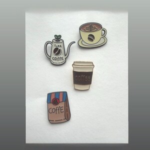 Könnte beinhalten: Eine Sammlung von Anstecknadeln zum Thema Kaffee. Die Anstecknadeln umfassen eine Kaffeekanne mit dem Wort "COFFE" und "luck", eine Kaffeetasse mit Latte Art, einen Coffee-to-go-Becher und einen Kaffeebeutel mit dem Wort "COFFE".