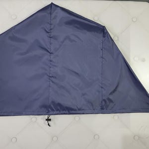 Könnte beinhalten: Eine dunkelblaue, dreieckige Schutzhülle aus einem glatten, synthetischen Material. Der Artikel verfügt über eine mittlere vertikale Naht und einen schwarzen, verstellbaren Kordelzug am unteren Rand, der dazu dient, den Stoff zu fixieren.