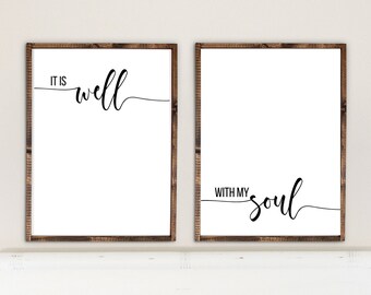 May include: Two framed prints with black calligraphy on a white background. The top print reads "It is well" and the bottom print reads "With my soul". The prints are hanging above a white headboard with a striped pillow that reads "Let's Cuddle".