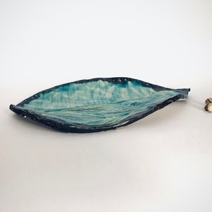 May include: A blue and white ceramic leaf-shaped serving dish with a textured surface. The dish is slightly curved and has a dark blue rim.