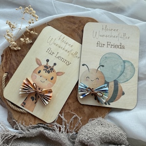 May include: Two wooden gift cards with illustrations and text. One card features a giraffe with a paper bow, the other a bee with a paper bow. The text on the cards reads "Kleiner Wunscherf&uuml;ller f&uuml;r Lenny" and "Kleiner Wunscherf&uuml;ller f&uuml;r Frieda".