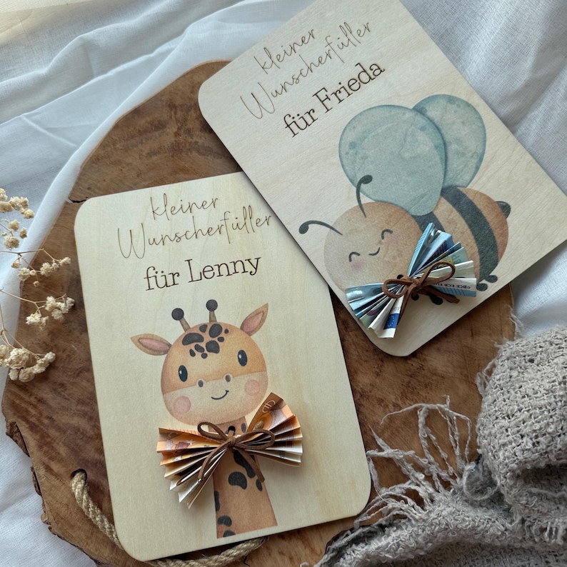 May include: Two wooden cards with illustrations and text. One card features a giraffe, the other a bee with blue wings. Both cards have folded paper bows and the text "kleiner Wunscherf&uuml;ller f&uuml;r Lenny" and "kleiner Wunscherf&uuml;ller f&uuml;r Frieda".