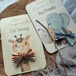 May include: Two wooden gift cards with illustrations and text. One card features a giraffe with a paper bow, the other a bee with paper wings. The text on the cards reads "kleiner Wunschf&uuml;ller f&uuml;r Lenny" and "kleiner Wunschf&uuml;ller f&uuml;r Frieda".