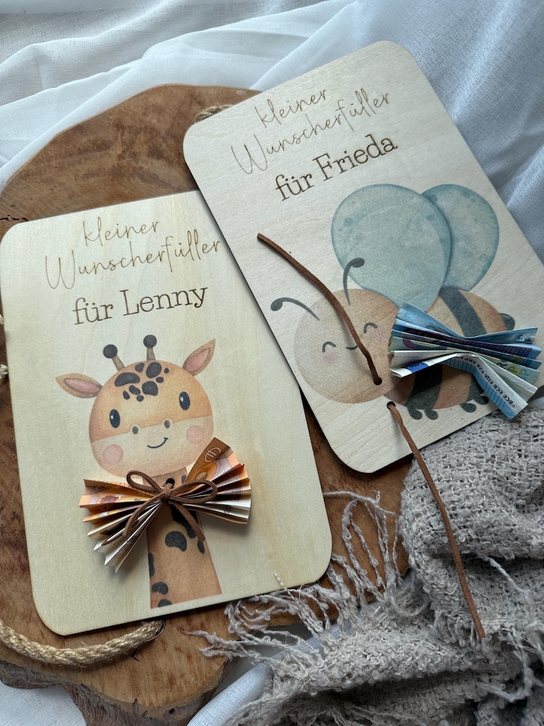 May include: Two wooden gift cards with illustrations and text. One card features a giraffe with a paper bow, the other a bee with paper wings. The text on the cards reads "kleiner Wunschf&uuml;ller f&uuml;r Lenny" and "kleiner Wunschf&uuml;ller f&uuml;r Frieda".