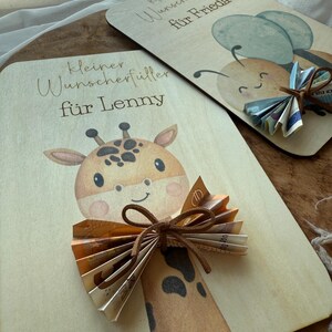 May include: Two wooden gift cards with illustrations and text. One card features a giraffe with a paper bow, the other a bee with paper wings. The text on the cards reads "Kleiner Wunschf&uuml;ller f&uuml;r Lenny" and "Kleiner Wunschf&uuml;ller f&uuml;r Frieda".