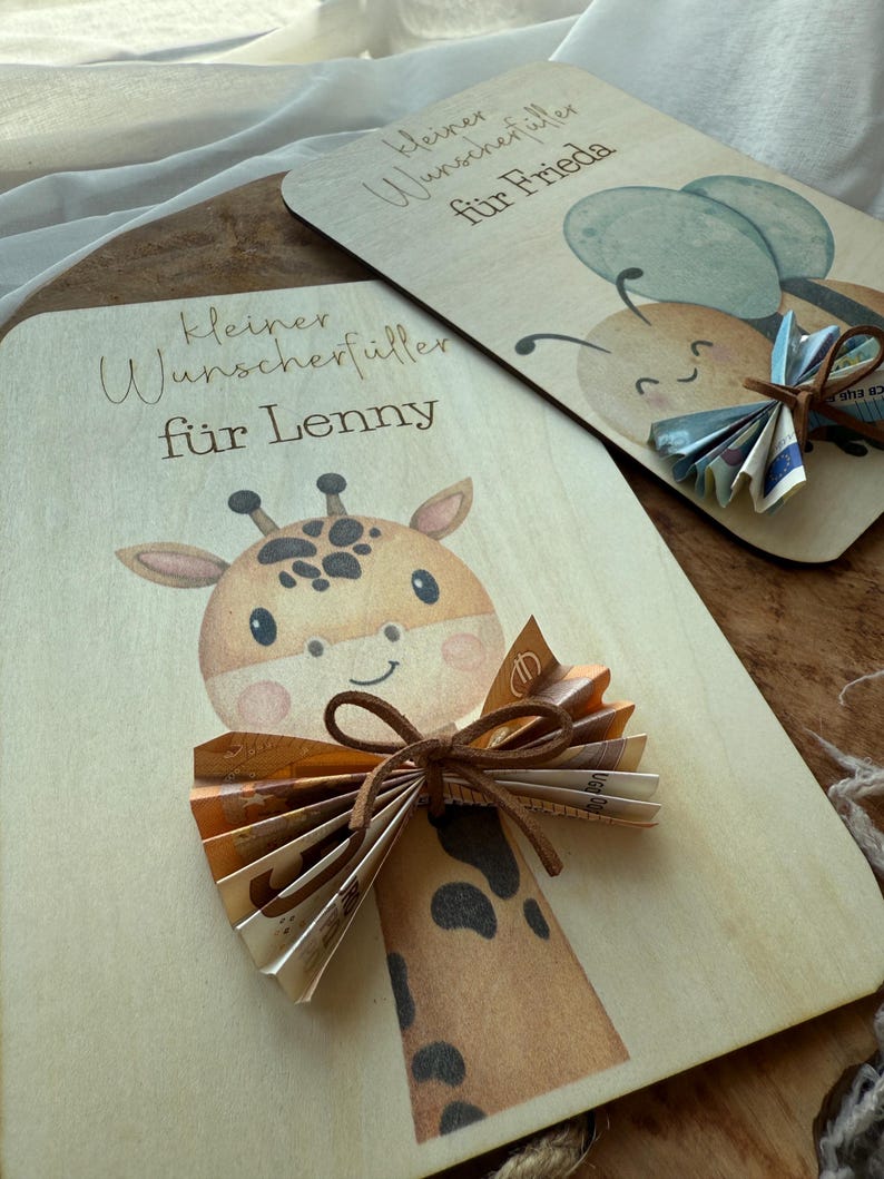 May include: Two wooden gift cards with illustrations and text. One card features a giraffe with a paper bow, the other a bee with paper wings. The text on the cards reads "Kleiner Wunschf&uuml;ller f&uuml;r Lenny" and "Kleiner Wunschf&uuml;ller f&uuml;r Frieda".