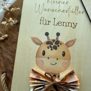 May include: A wooden plaque with a giraffe illustration and the text "kleiner Wunscherf&uuml;ller f&uuml;r Lenny". The giraffe has brown spots and a bow made of folded banknotes.