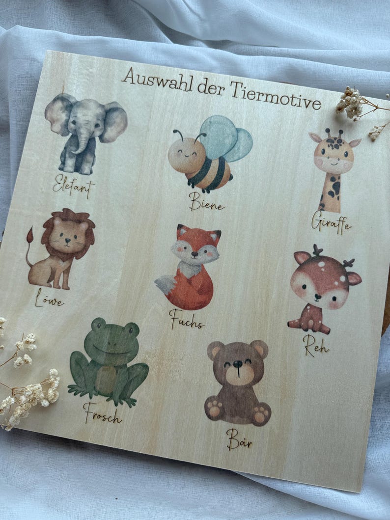 May include: Wooden board featuring watercolor illustrations of various animals, including an elephant, bee, lion, fox, frog, bear, giraffe, and deer. The text "Auswahl der Tiermotive" is printed at the top.