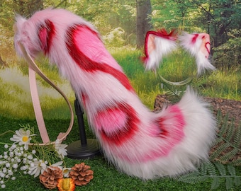 May include: Pink and red fluffy tail with a white tip, attached to a brown leather strap. The tail is a costume accessory for a cat or other animal.