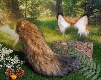 May include: A brown and black faux fur tail with a tan leather strap. The tail is on a green grassy surface. A pair of fox ears are in the background.