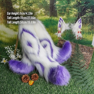 Puede incluir: Dos colas esponjosas blancas y moradas con una punta morada. Las colas miden aproximadamente 70 cm y 50 cm de largo. Las colas están sobre una superficie de hierba verde con un tronco marrón en el fondo.