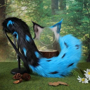 Puede incluir: Un conjunto de cola y orejas de piel sintética azul y negra. La cola es principalmente azul con manchas negras y una correa negra. Las orejas son azules, negras y blancas. El conjunto está diseñado para cosplay o disfraces.