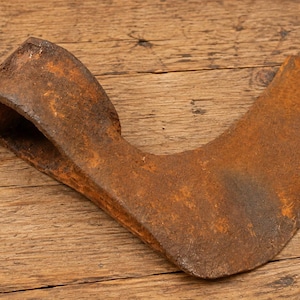 May include: A weathered, rusted iron axe head featuring a curved blade and a hollow, rectangular socket for a handle. The metal surface displays a deep orange and brown patina with visible oxidation throughout the entire object's structure.