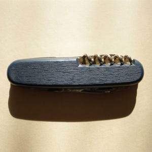 May include: A navy blue pocket knife with a gold-coloured corkscrew. The knife has a textured surface and a silver blade. The corkscrew is visible on the top of the knife.
