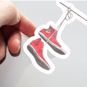Op de afbeelding: Een paar rode high-top sneakers met witte veters die aan een touwtje hangen.