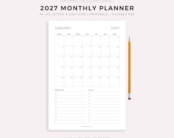 May include: A white 2027 monthly planner with a January calendar layout, priorities, and to-do list sections. The planner includes the text "2027 MONTHLY PLANNER" and "PRINTABLE + FILLABLE PDF". A yellow pencil is placed on the right side.