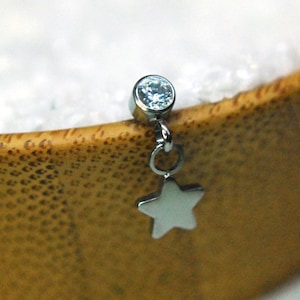 Könnte beinhalten: Ein Körperschmuckstück aus Silber mit einem klaren Stein und einem baumelnden Sternanhänger.