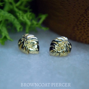 May include: A pair of gold-colored earrings featuring a detailed monstera leaf design.