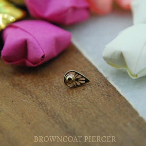 May include: A gold nose piercing with a teardrop design and a small ball at the top.