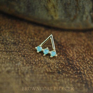 May include: Gold triangle body jewelry with three light blue opal stones.