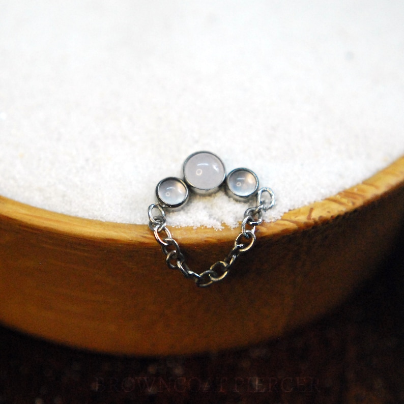 Pode incluir: Uma corrente de prata com tr&ecirc;s pedras brancas que parecem opalas, a pedra central &eacute; maior do que as duas de cada lado.