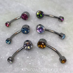 Può includere: Sei gioielli per il corpo a barra curva con aste metalliche ed estremità circolari dotate di cristalli sfaccettati nei colori rosa, iridescente, blu, viola, trasparente e ambra. Il testo BROWNCOAT PIERCER è stampato nella parte inferiore.