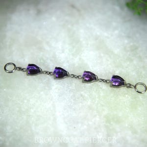 May include: A dark metal chain featuring four teardrop-shaped purple amethyst stones set in prongs. The chain includes a circular ring at each end for attachment. The text BROWNCOAT PIERCER is visible at the bottom of the image.