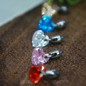 May include: A line of heart-shaped crystal charms in various colours, including red, pink, white, blue, and yellow, attached to silver-toned posts. The charms are arranged in a line, with the red charm at the bottom and the yellow charm at the top.
