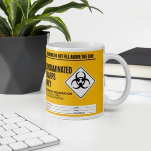 May include: A white ceramic mug with a yellow and black warning label that reads "WARNING DO NOT FILL ABOVE THE LINE CONTAMINATED SHARPS ONLY DESTROY BY INCENERATION OR OTHER SUITABLY AUTHORISED PROCESS Date. Date. Dept/Ward."