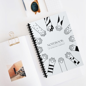 May include: A white spiral bound notebook with black paw prints and the text "Notebook of Veterinary Gibberish".