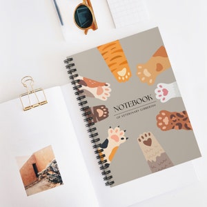 May include: A spiral bound notebook with a light brown cover featuring a whimsical design of colorful cat paws. The text "NOTEBOOK OF VETERINARY GIBBERISH" is printed on the cover.