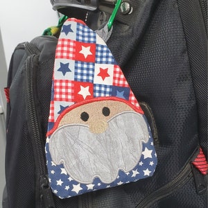 May include: A red, white, and blue patchwork gnome-themed bag charm with a white star pattern and a gray embroidered beard.