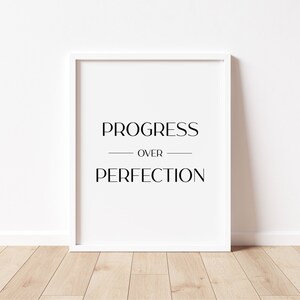 May include: A white framed print with the text "PROGRESS OVER PERFECTION" in black lettering.