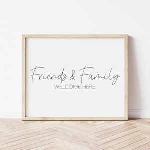 May include: A framed print with the text "Friends & Family WELCOME HERE" in a simple, modern font. The frame is light wood and the background is white.