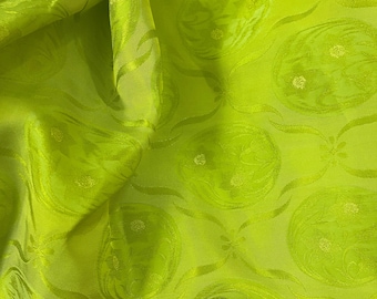 May include: Vibrant lime green fabric featuring a repeating pattern of swirling floral and paisley-like designs. The fabric has a subtle sheen, creating highlights and shadows that emphasise the texture and pattern. The overall effect is a luxurious and decorative textile.