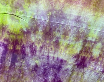 May include: Abstract tie-dye fabric with a purple and green color scheme. The fabric has a mottled appearance with shades of light and dark purple and green.
