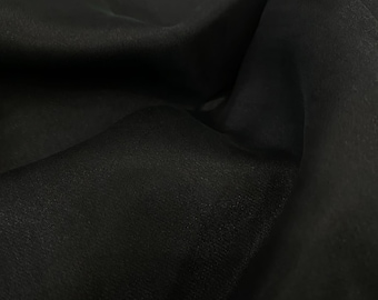 May include: Black sheer fabric with a smooth, silky texture. The fabric is draped and folded, creating soft, flowing lines.