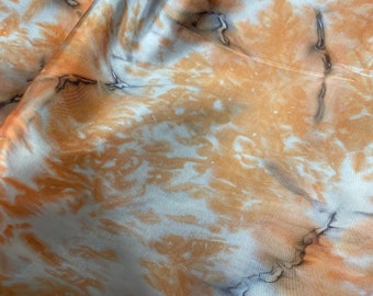 May include: A white fabric with a tie-dye pattern in shades of orange and brown.