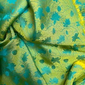 Könnte beinhalten: Nahaufnahme eines gefalteten Stoffes mit floralem Muster. Der Stoff hat eine gelb-grüne Grundfarbe mit einem türkisfarbenen Blumendesign. Die Ränder des Stoffes sind gelb. Der Stoff wird wahrscheinlich für Kleidung oder Heimdekoration verwendet.