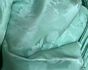 May include: A close-up of a light green fabric with a floral pattern. The fabric is soft and silky, and the flowers are embossed.