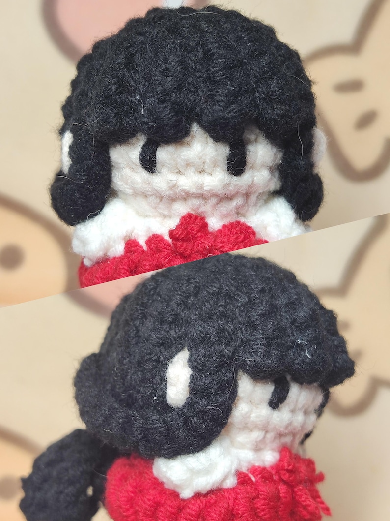 May include: A crocheted doll with black hair, a white face, and a red sweater. The doll is wearing a white scarf.