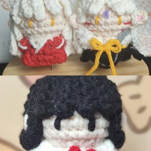 May include: Three crocheted plushies, two with white hair and red clothing, and one with black hair and red clothing. The plushies are handmade and have a cute, cartoon-like appearance.