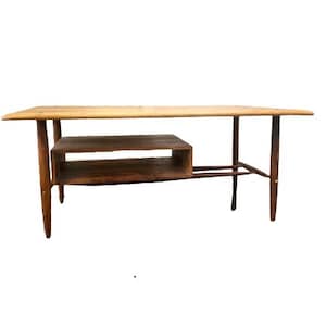 May include: A mid-century modern coffee table with a light wood top and a lower shelf. The table has a simple, elegant design with tapered legs.